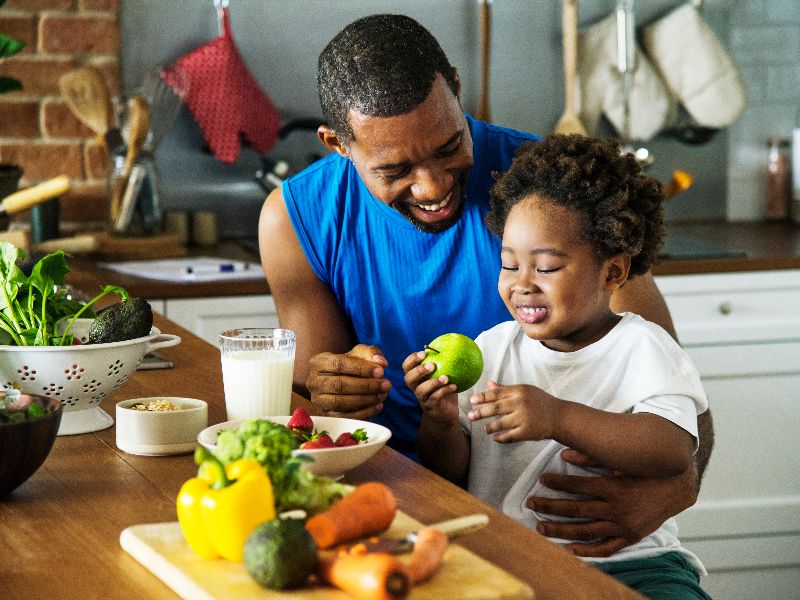 Father giving son apple seated by table in kitchen